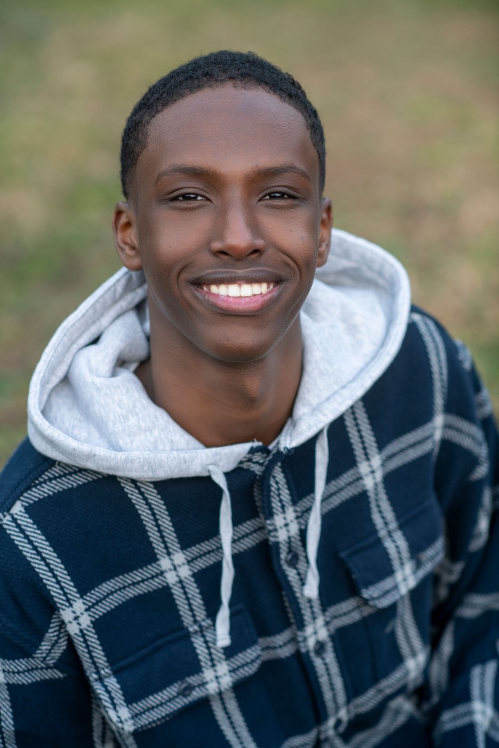 Smiling young Black man in a plaid hoodie outdoors, exuding confidence and joy.