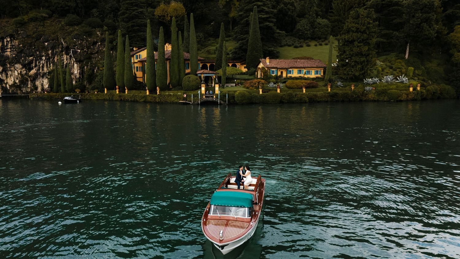A red and white speedboat glides across a tranquil lake surrounded by lush green trees and mountains.