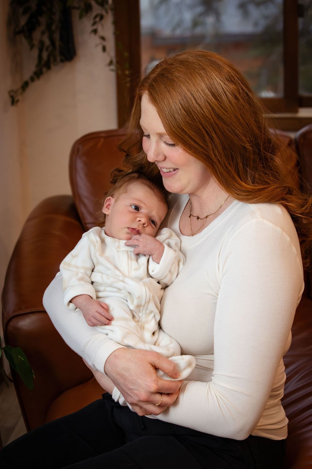Tender moment between parent and baby in matching white outfits on leather furniture.