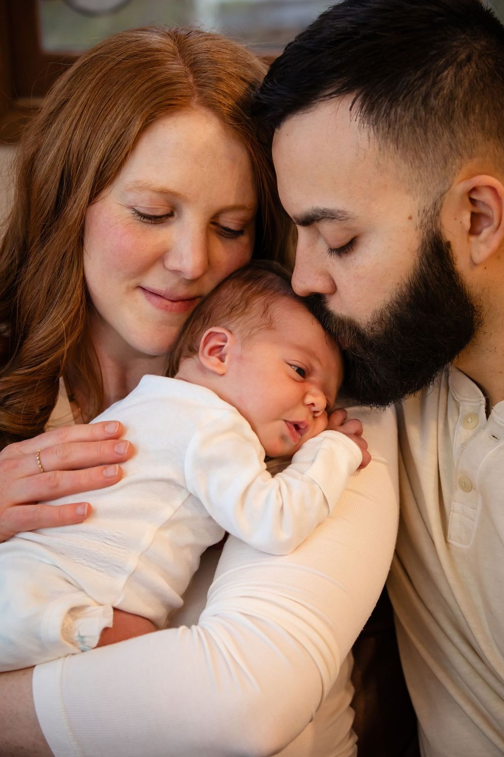 Intimate family moment captured with baby sleeping between parents on leather couch.