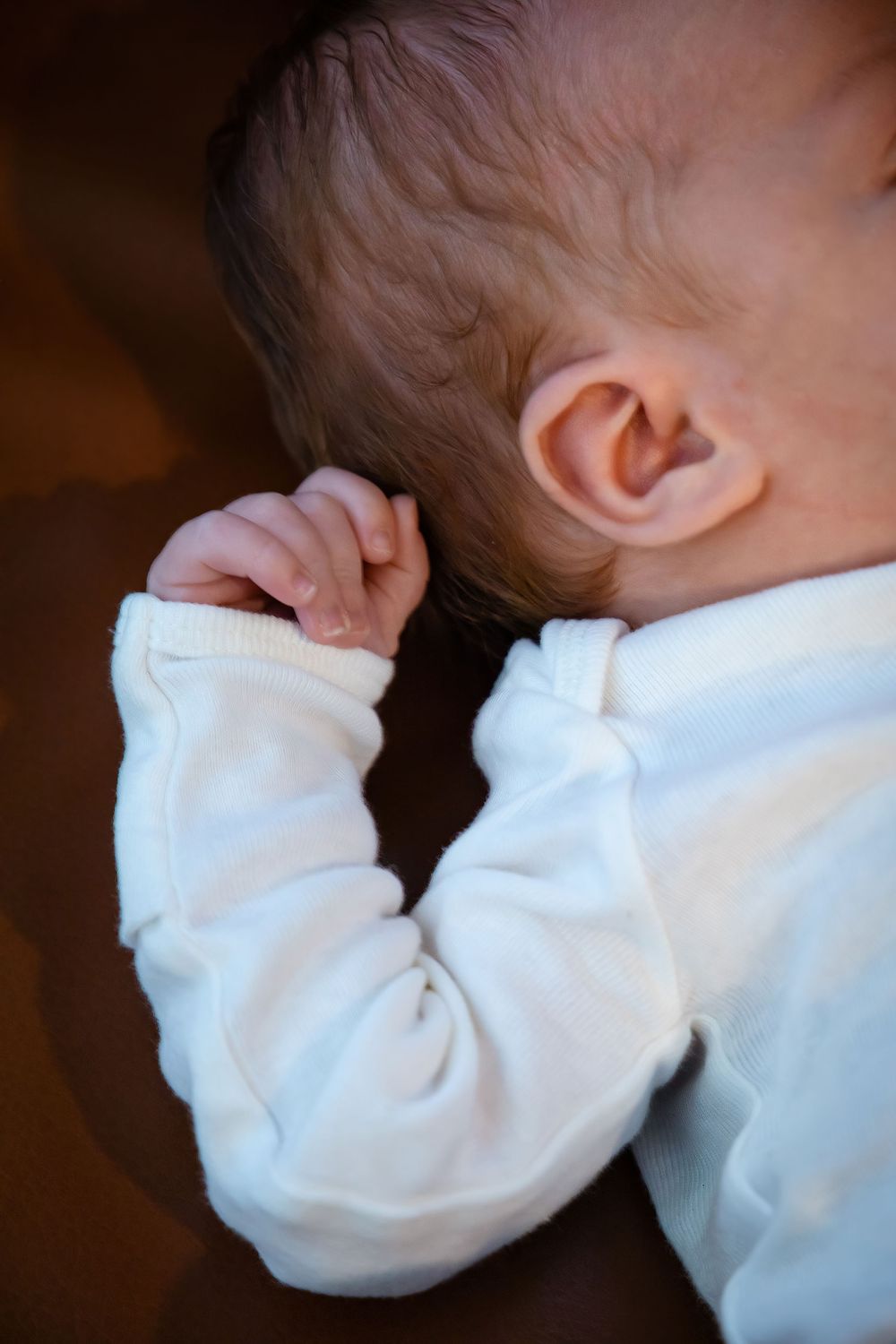 Close-up detail of baby wearing white sleeves against dark background.