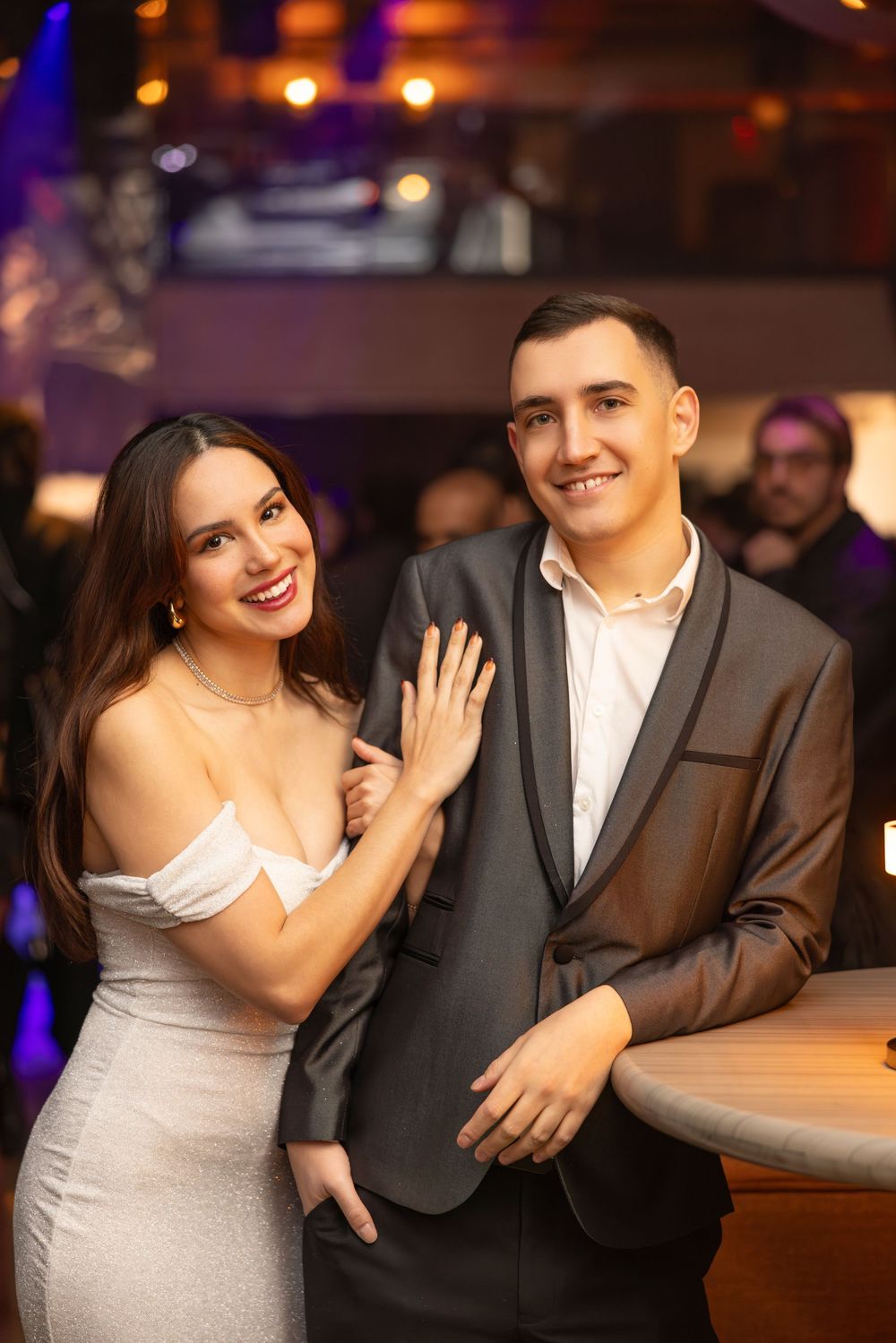 A couple shares romantic moments in formal attire at an elegant venue with warm lighting and blurred background decor.