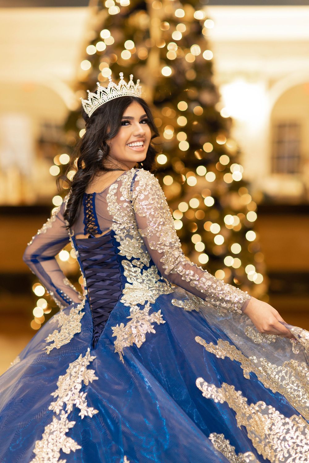 A stunning royal blue and gold quinceañera dress with intricate lace details sparkles against Christmas lights.