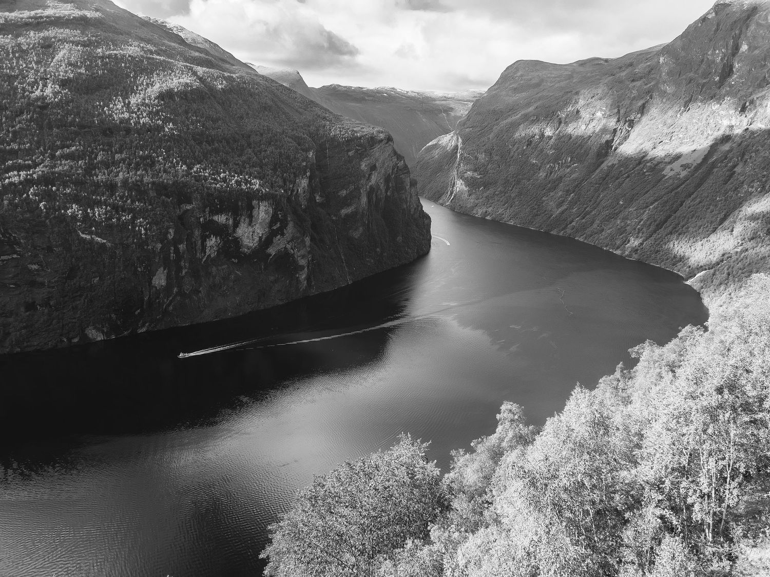 Dramatic black and white landscape of a Norwegian fjord surrounded by steep mountain cliffs.