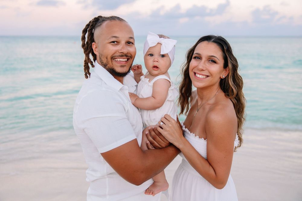 Family of three in white outfits playing on tropical beach at sunset.