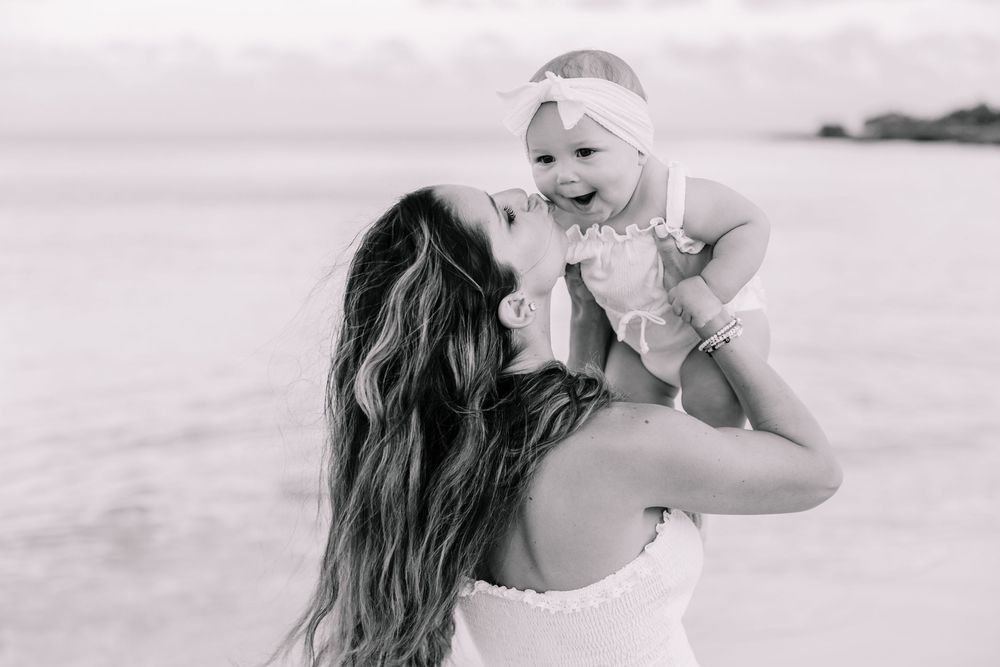 Mother and child sharing joyful moment on beach during sunset photoshoot.