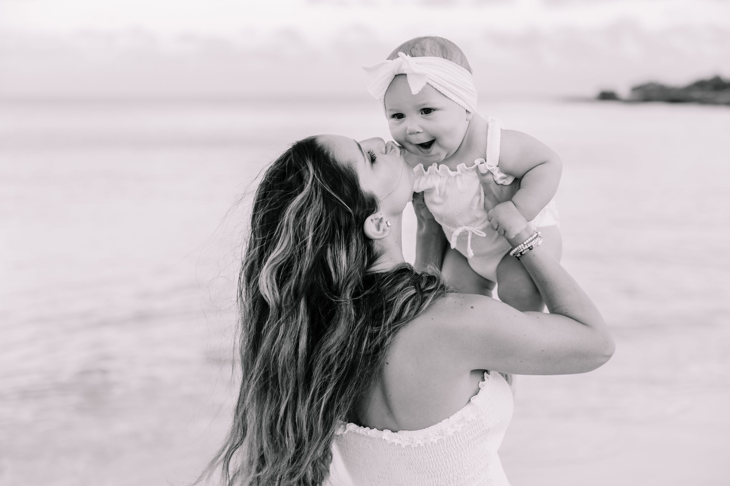 Mother and child sharing joyful moment on beach during sunset photoshoot.