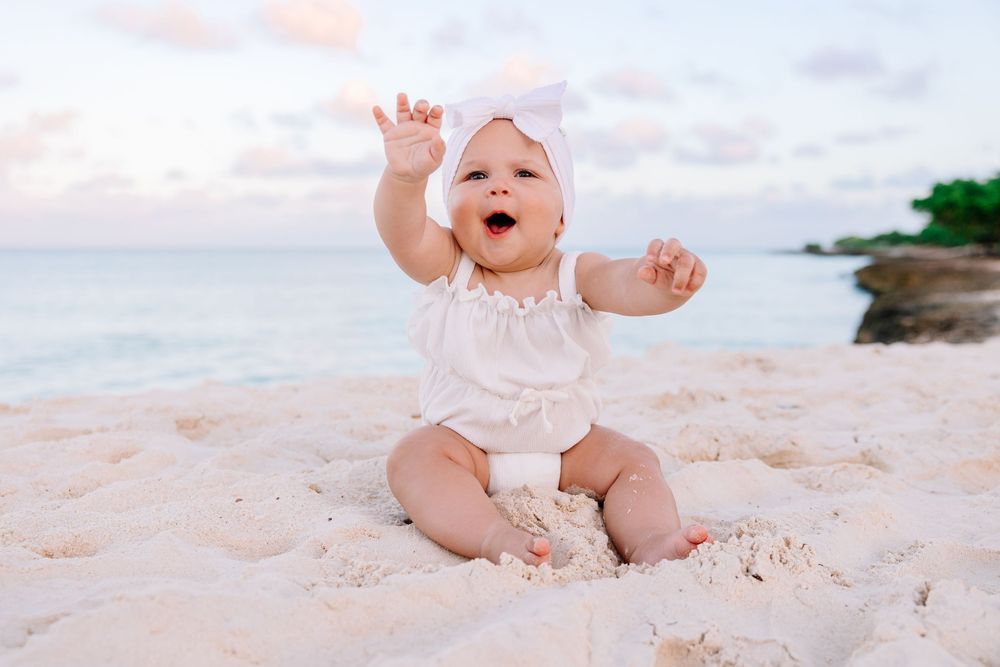 Baby playing and crawling on sandy beach at sunset with ocean waves in background.