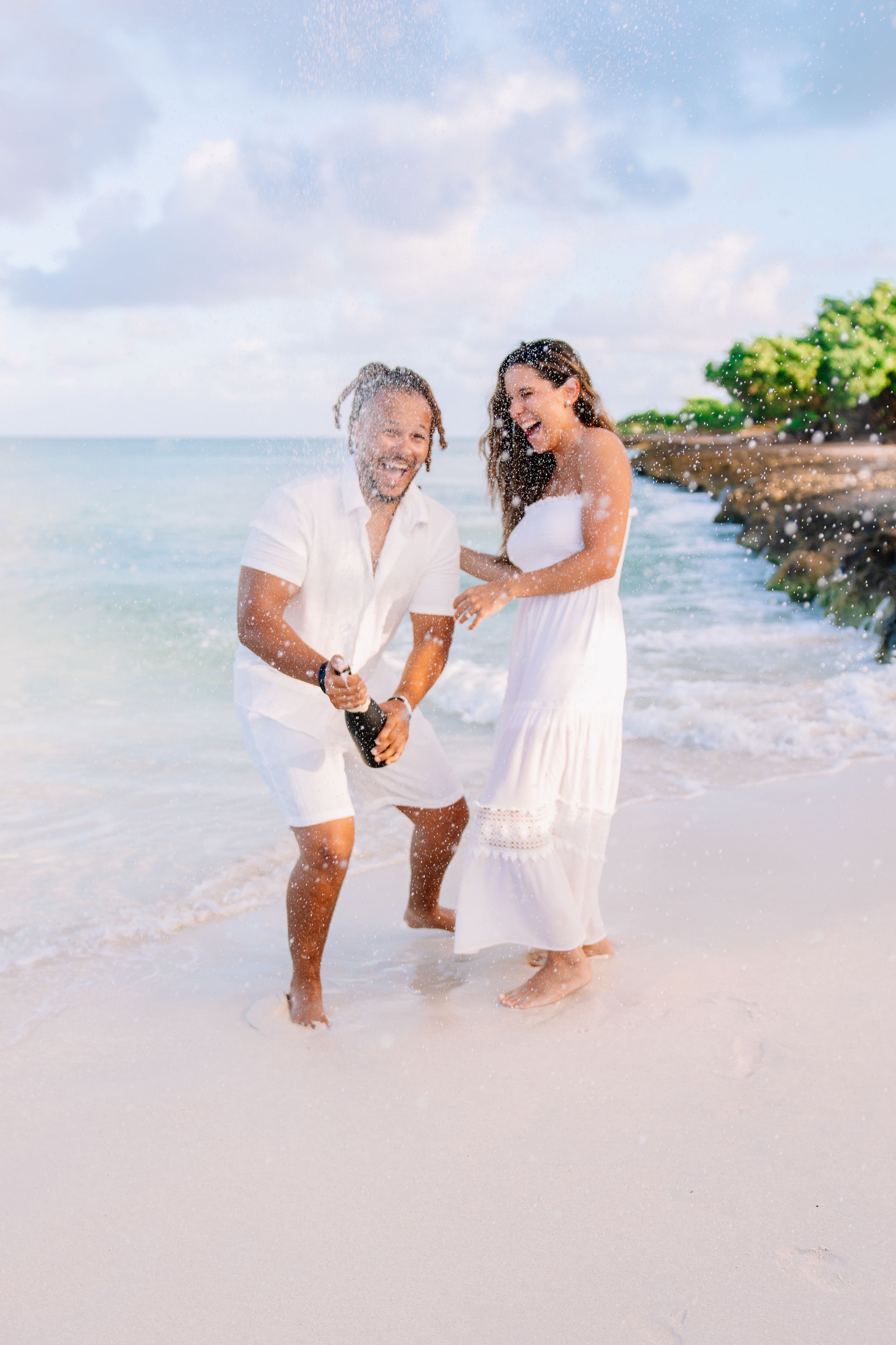 Family enjoying playful moments together on a tropical beach with white sand and ocean waves.