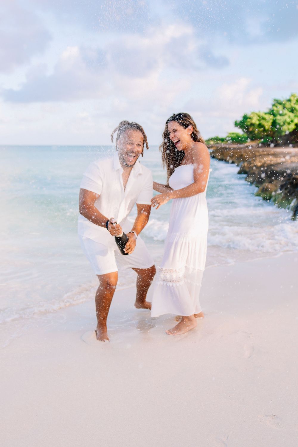 Family enjoying playful moments together on a tropical beach with white sand and ocean waves.