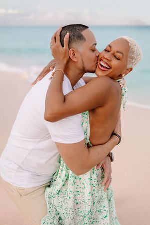 Romantic beach photoshoot with couple in casual summer attire sharing intimate moments.