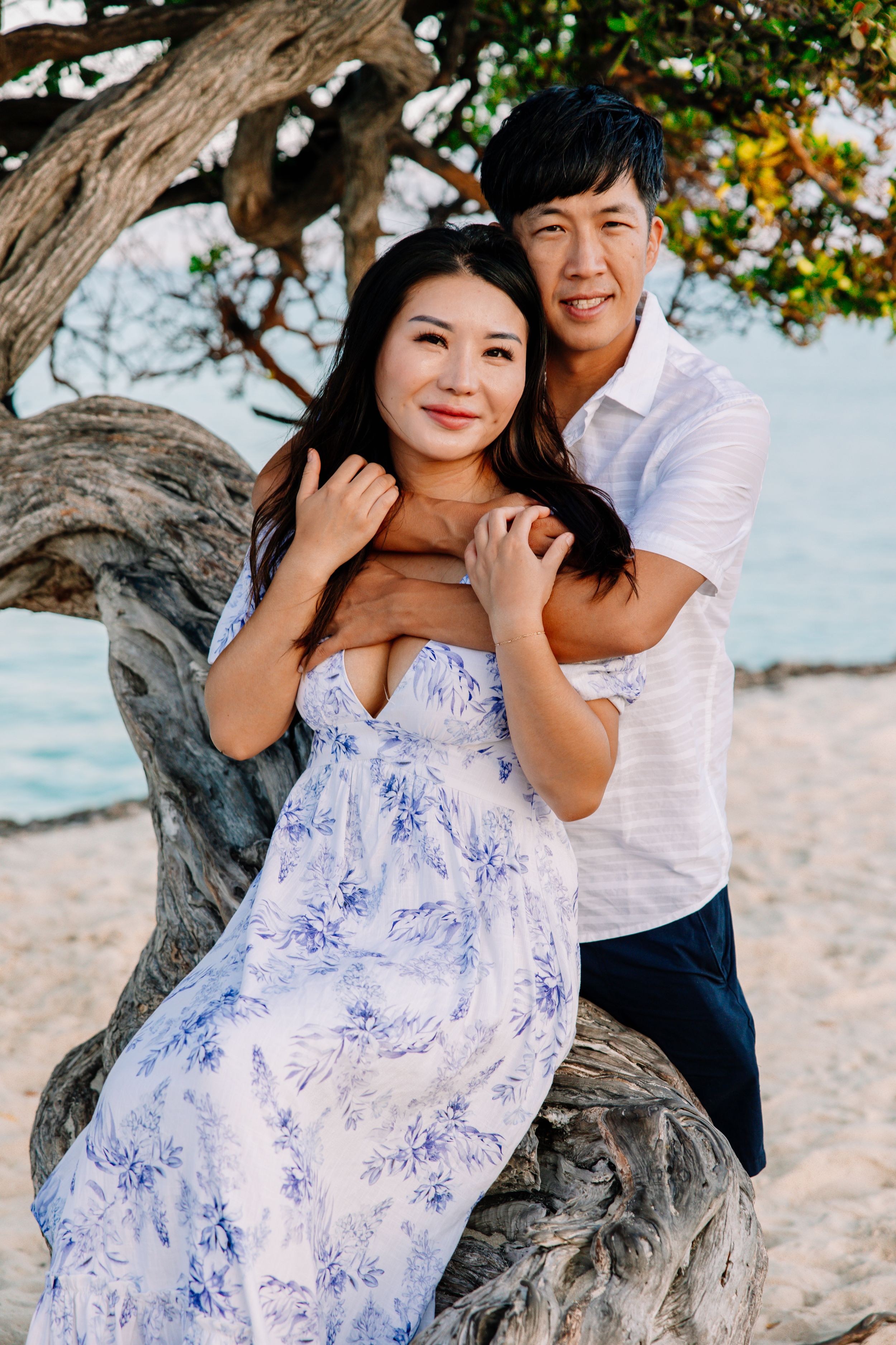 Couple sharing playful moments on beach while sitting on driftwood tree.