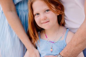 Young girl in blue dress smiling during outdoor family photoshoot.