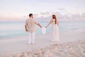 Couple in white outfits walking along a scenic beach at sunset.