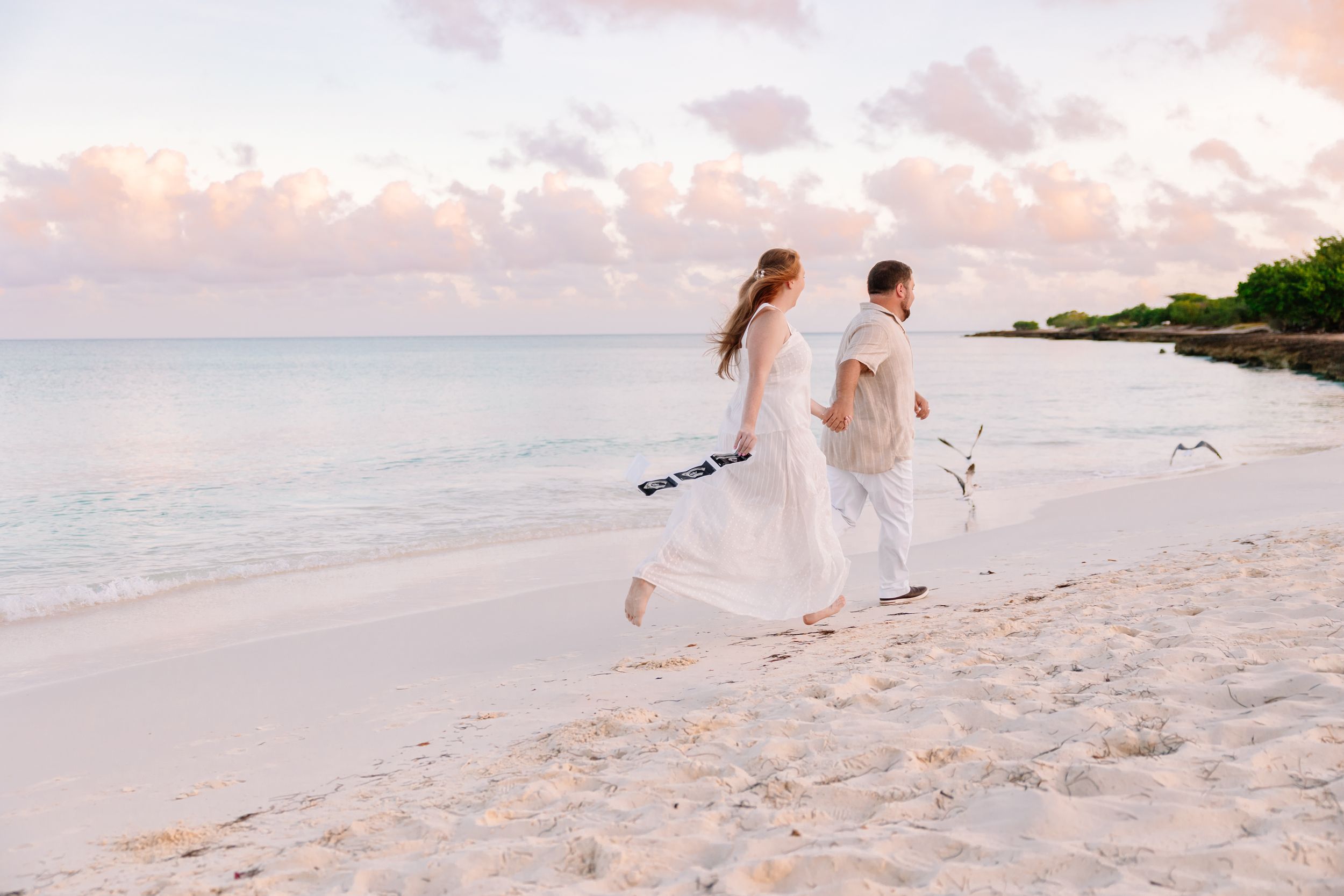 Romantic beach photoshoot with couple walking along shoreline at dusk.