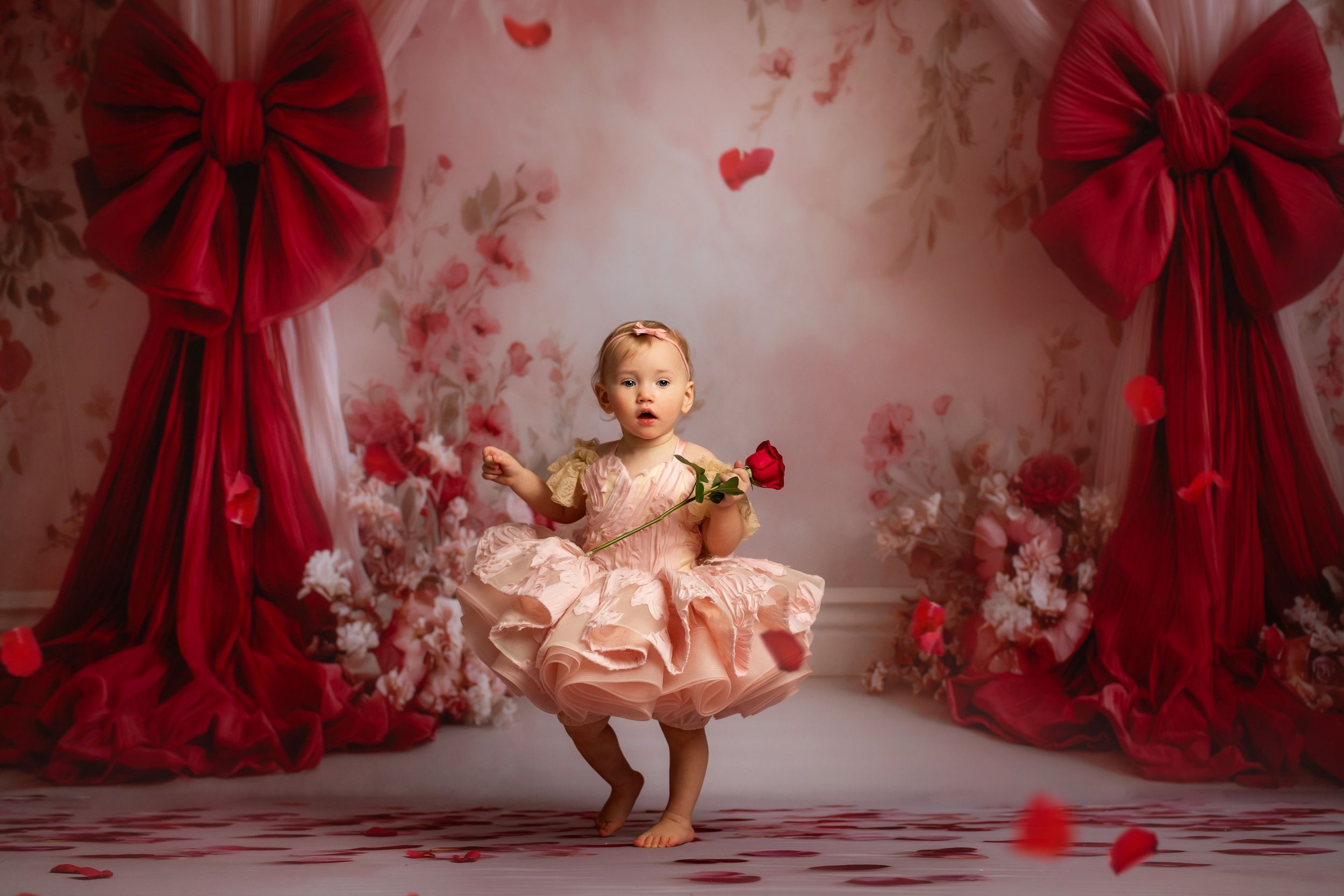 A small child twirls in a peach dress against a romantic backdrop with red bows and hearts for Valentine's Day.