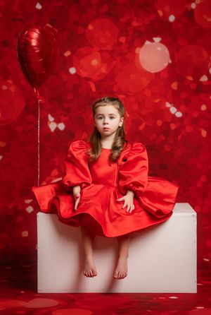A child in a vibrant red dress poses against a dreamy red bokeh background in a creative Valentine's Day photo session.