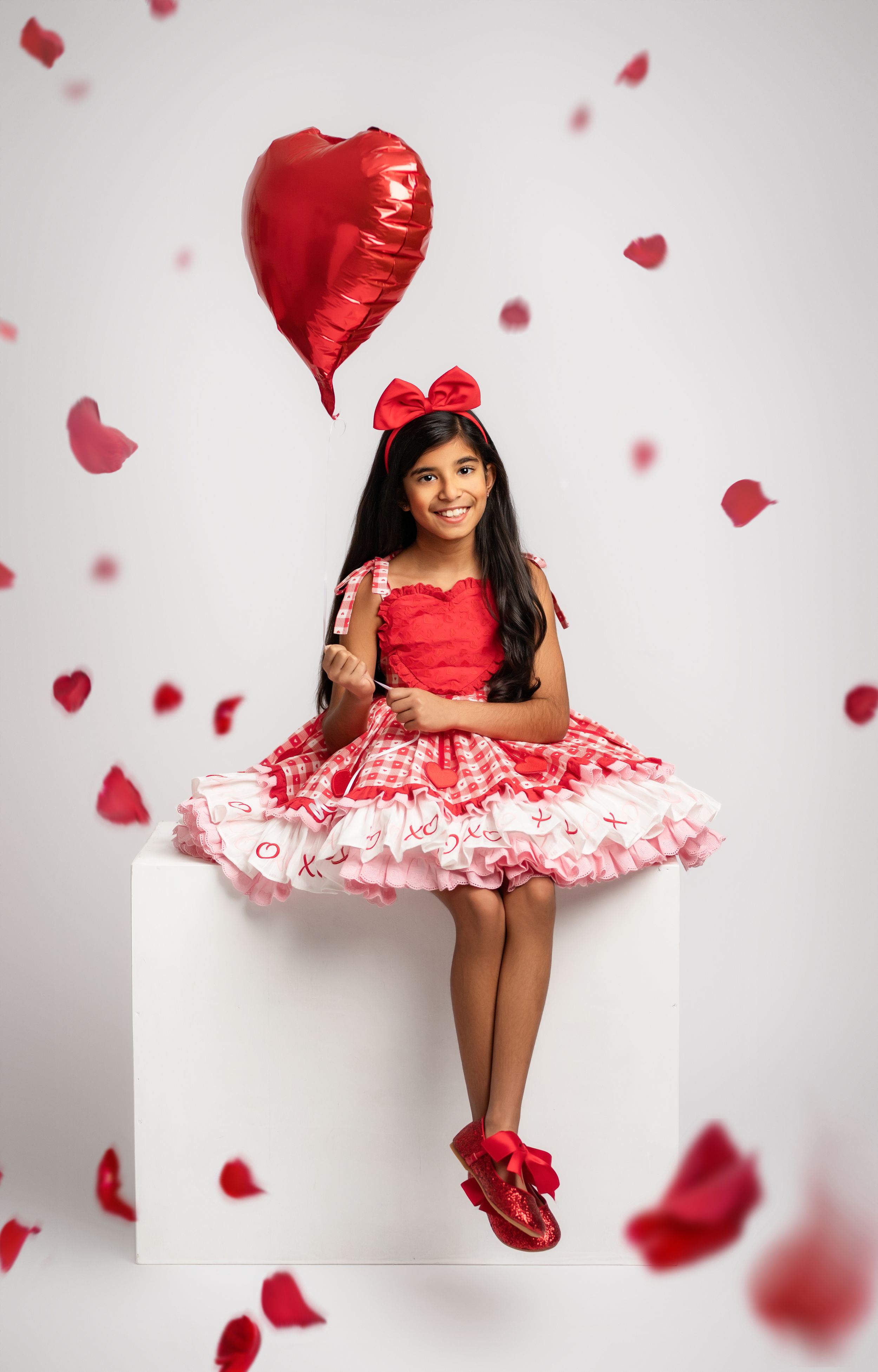 A red and white Valentine's themed photoshoot with falling heart petals and a decorative dress against a white backdrop.