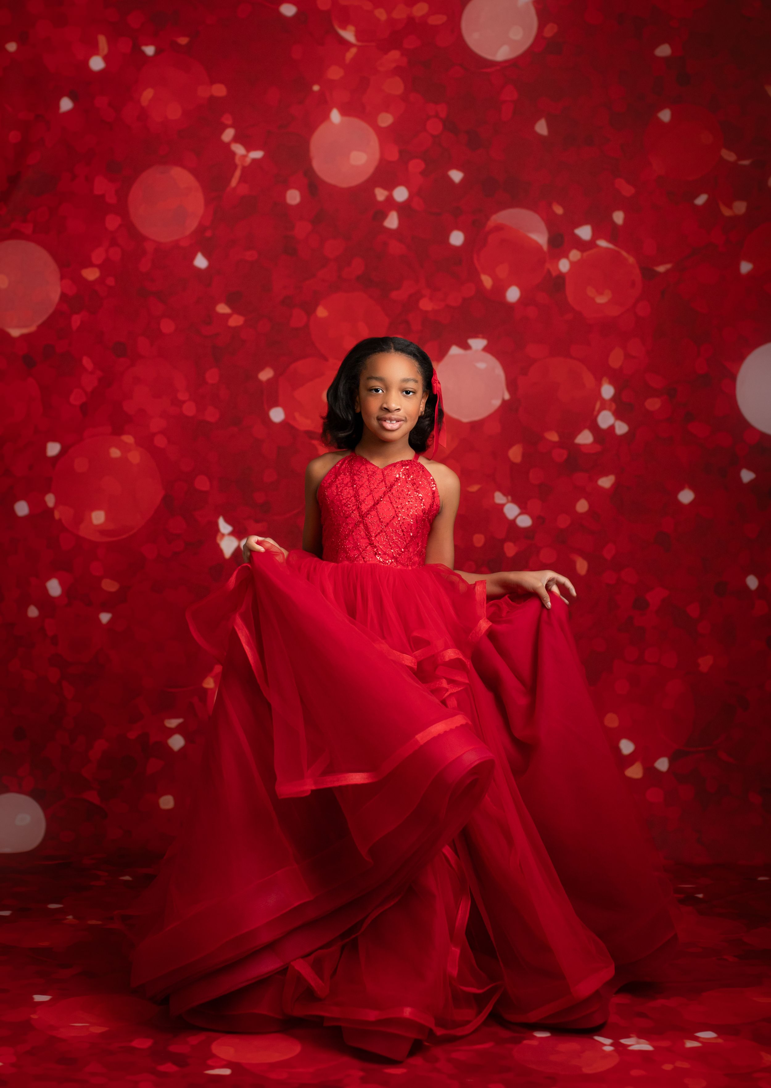 Young dancer in flowing red gown twirls gracefully against a festive red bokeh background.