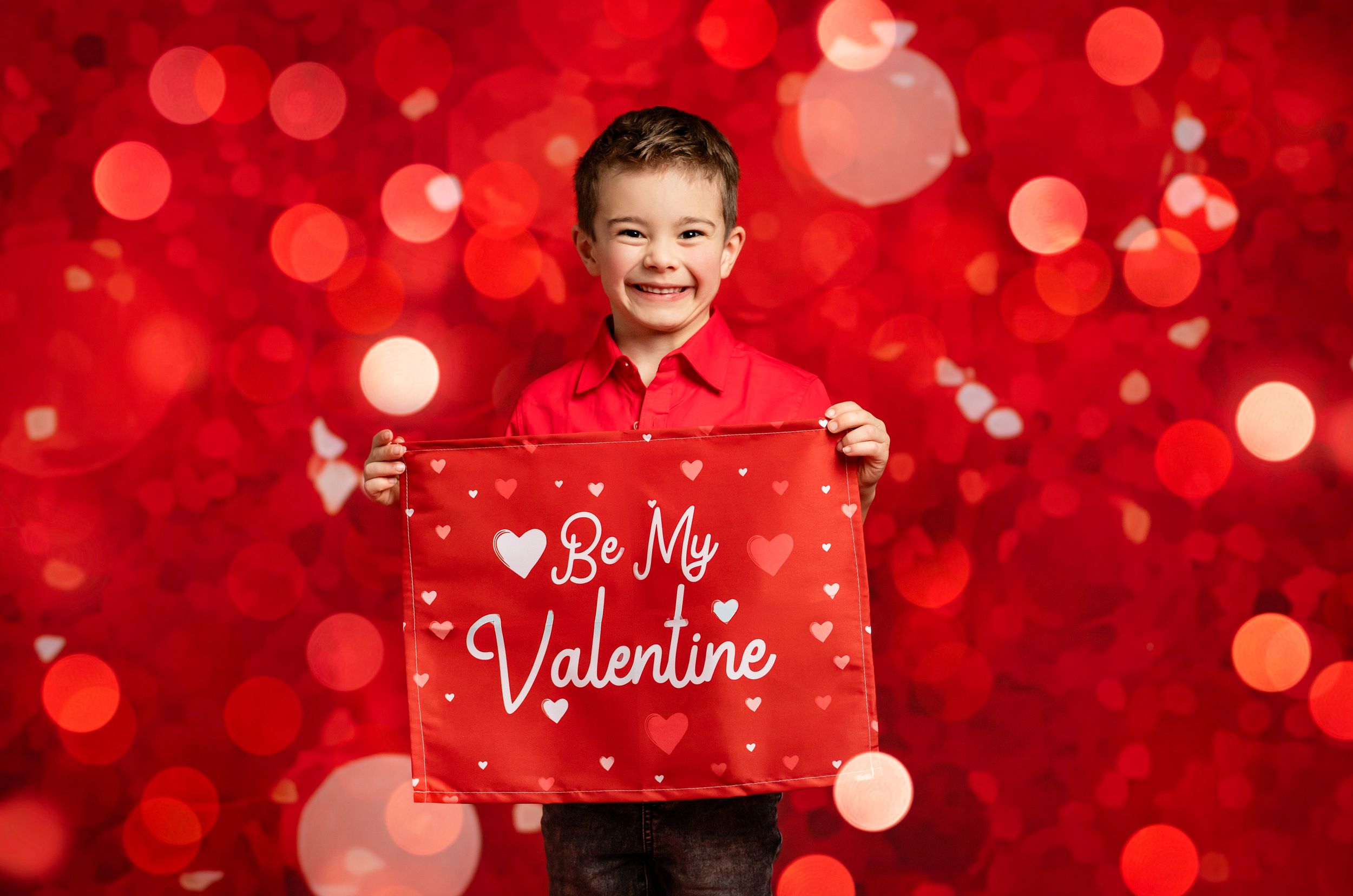 A person holds a red Valentine's Day sign with hearts and bokeh lights in the background.