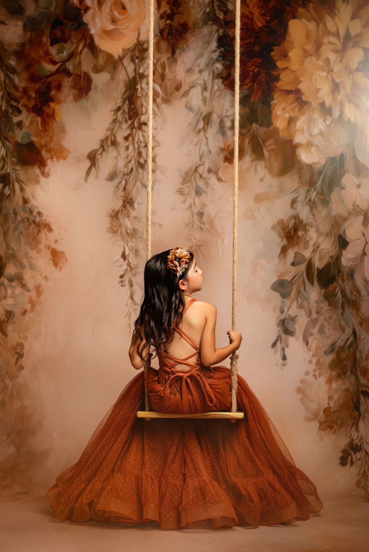 A sequence of romantic photos showing a person in a flowing rust-colored dress sitting on a decorative swing against a floral backdrop.