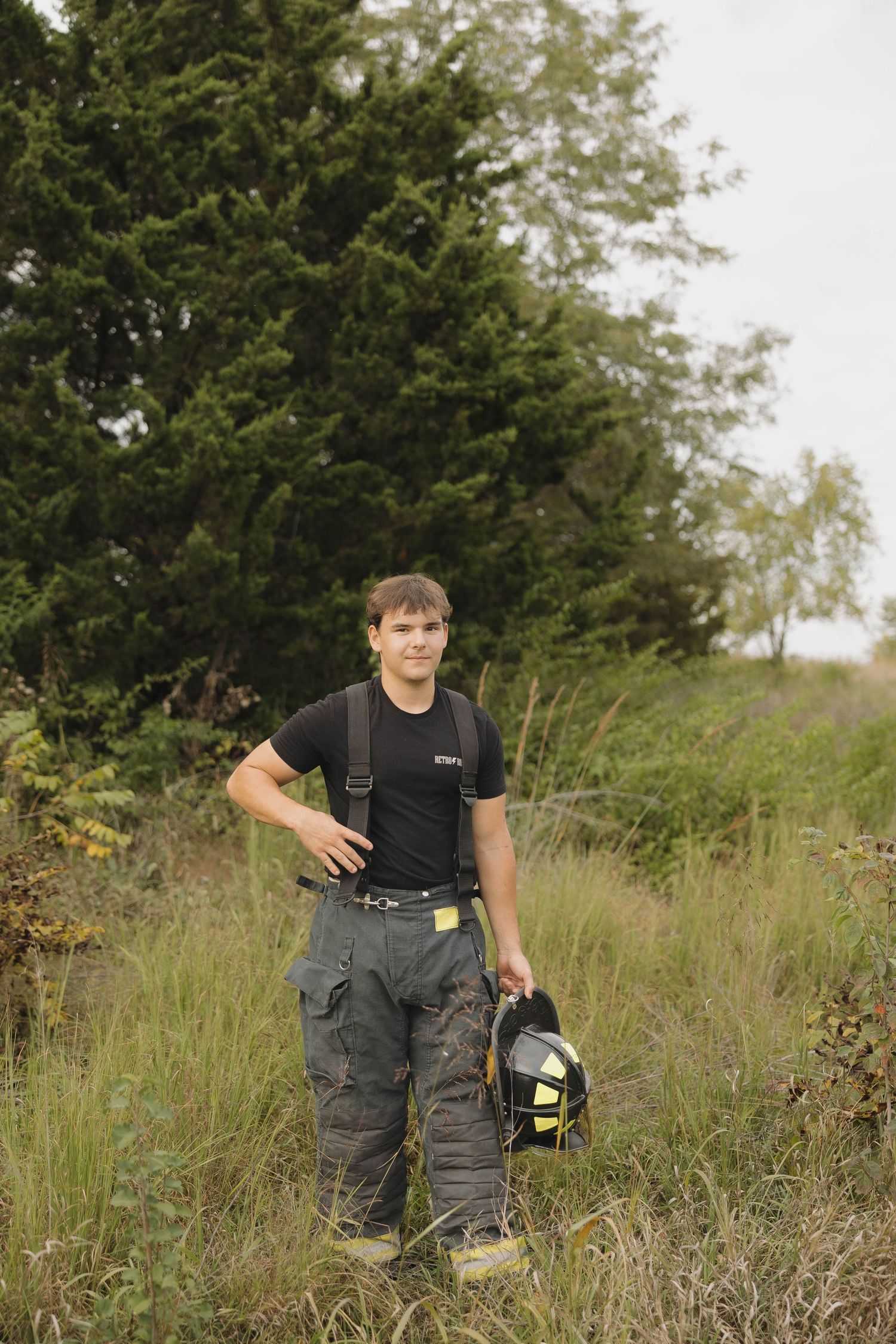 Person in black shirt and gray pants walking through meadow with camera equipment.