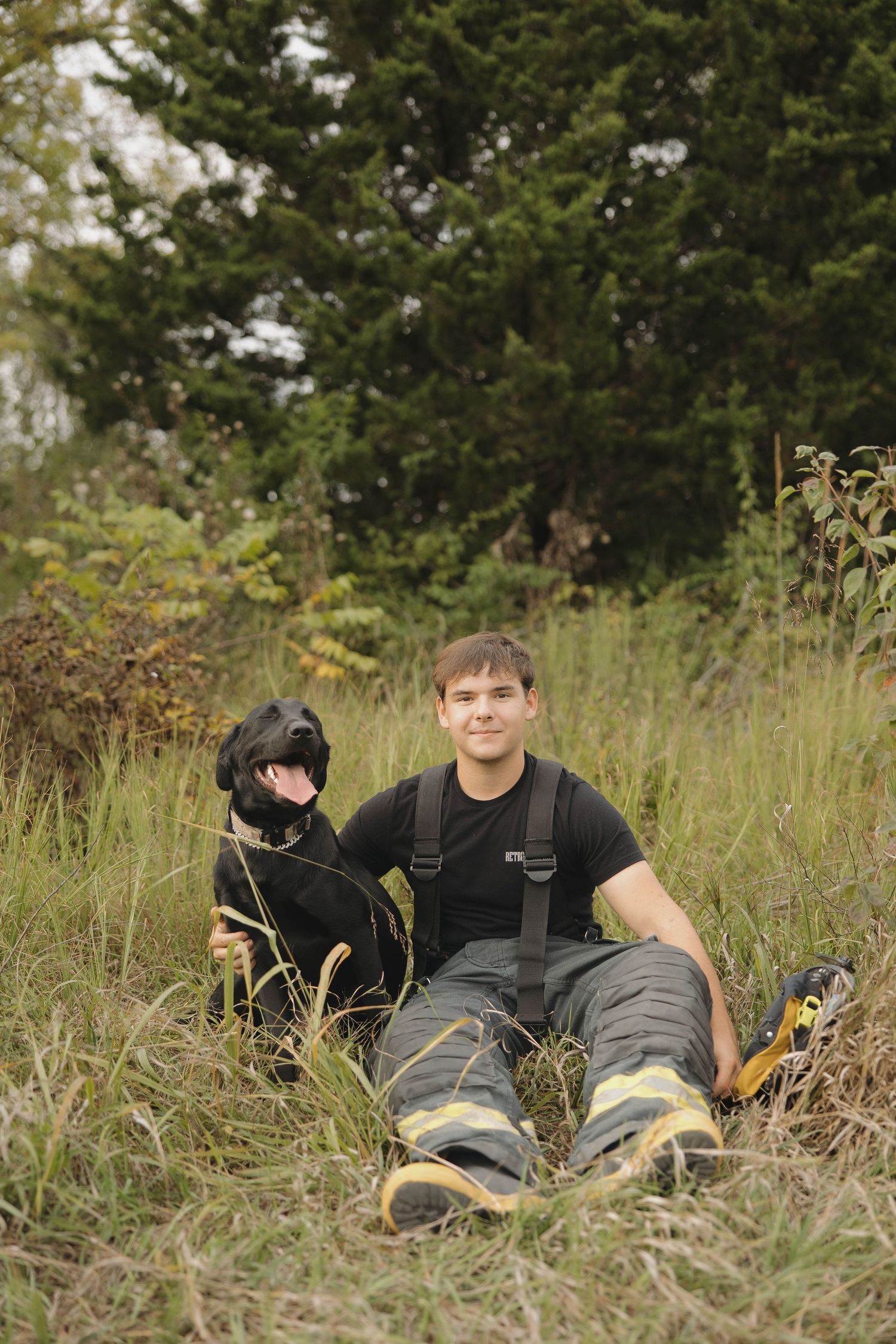Two people relax in tall grass on a sunny day with evergreen trees in the background.