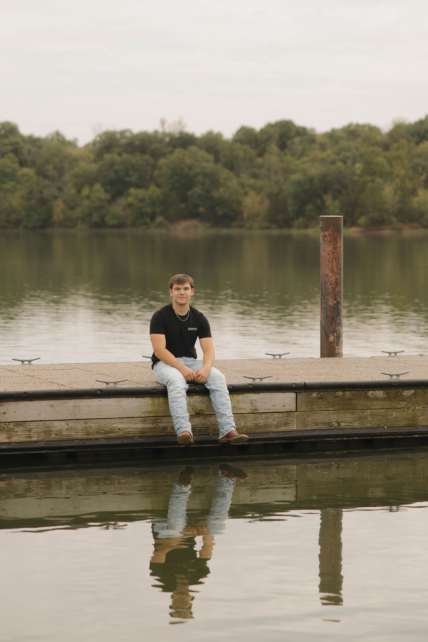 Person sitting on a wooden dock by a tranquil lake surrounded by autumn trees.