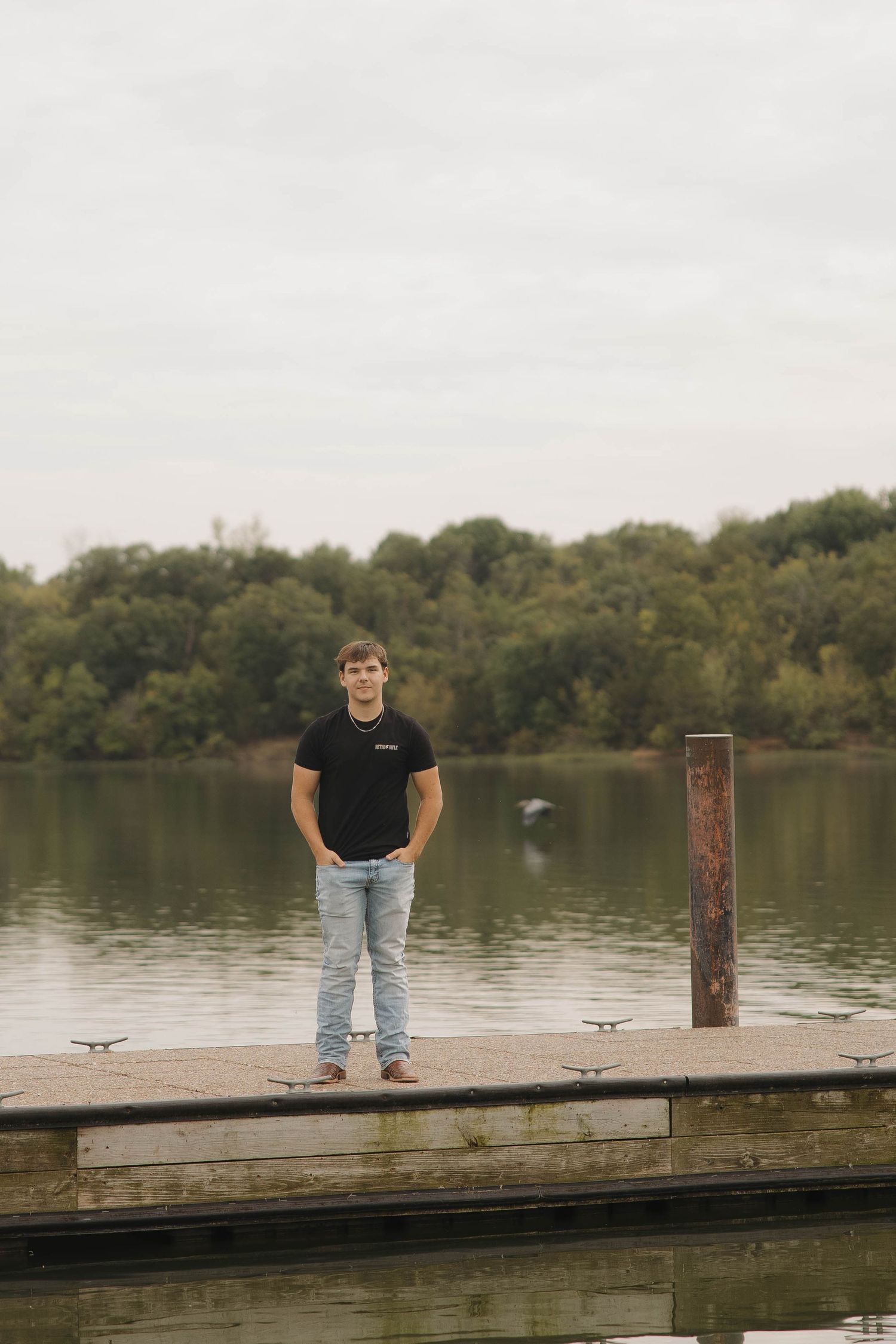Person standing on a wooden dock overlooking a serene lake surrounded by trees.