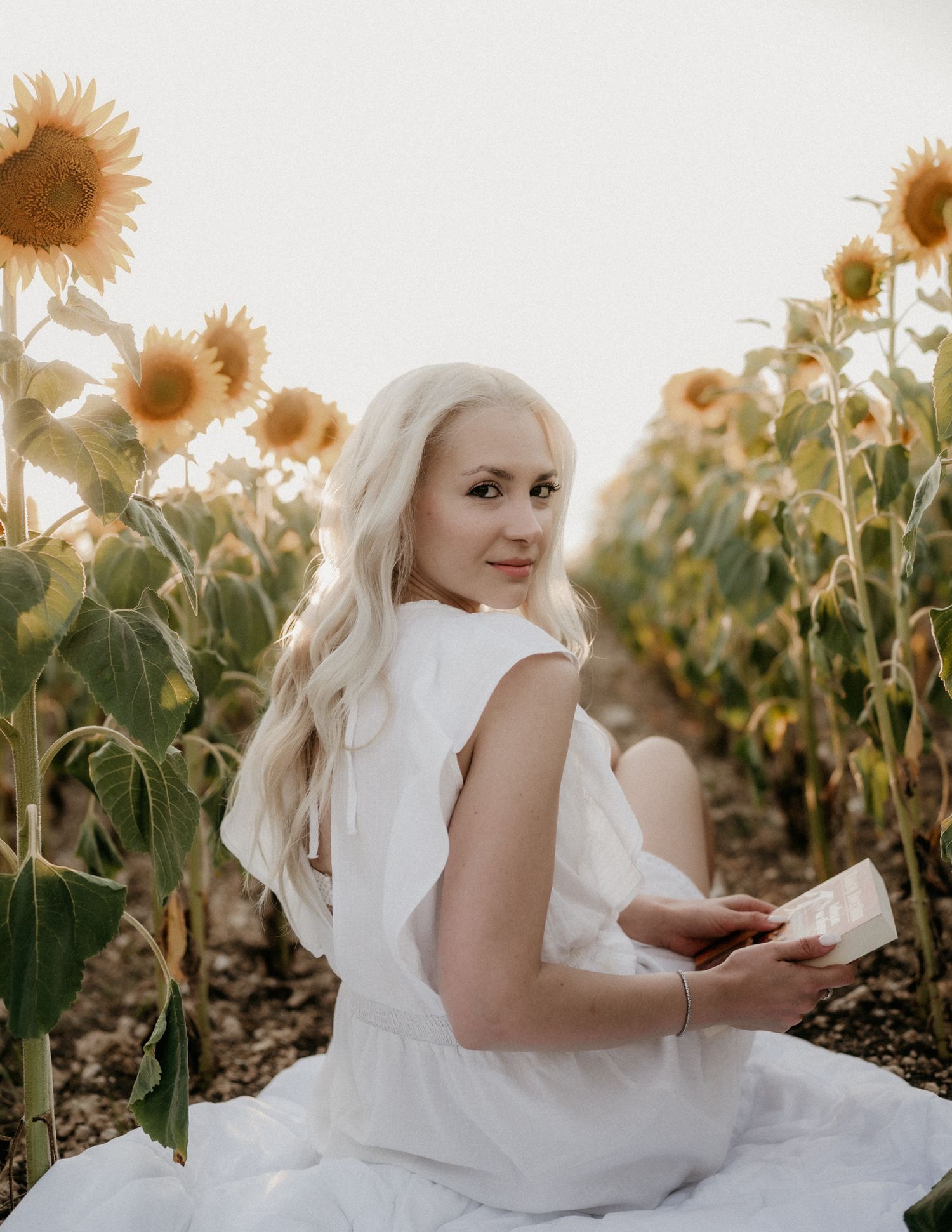 A person in white dress lies gracefully among tall sunflowers in a field.