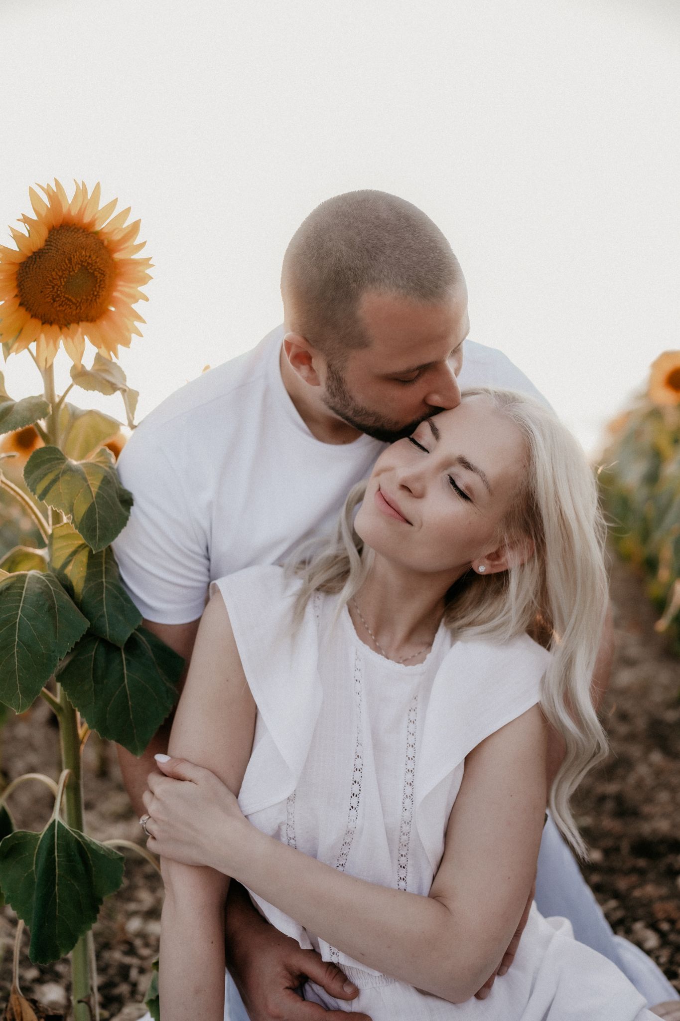 Romantic couple embracing in a sunflower field at sunset, creating a dreamy summer atmosphere.