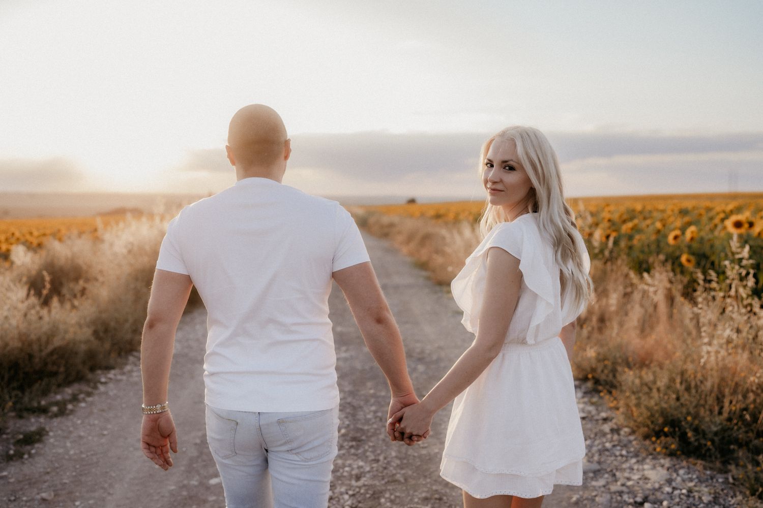 A couple walks hand in hand through a sunflower field at golden hour.