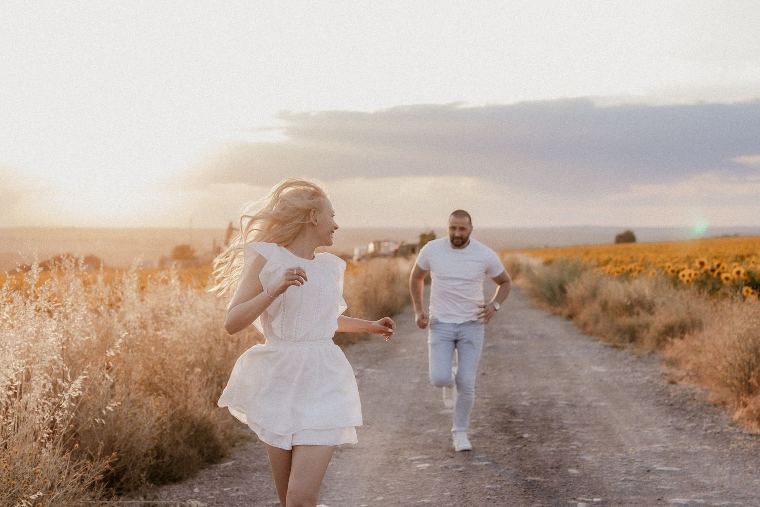 A couple walking together on a dirt path through a golden desert landscape at sunset.