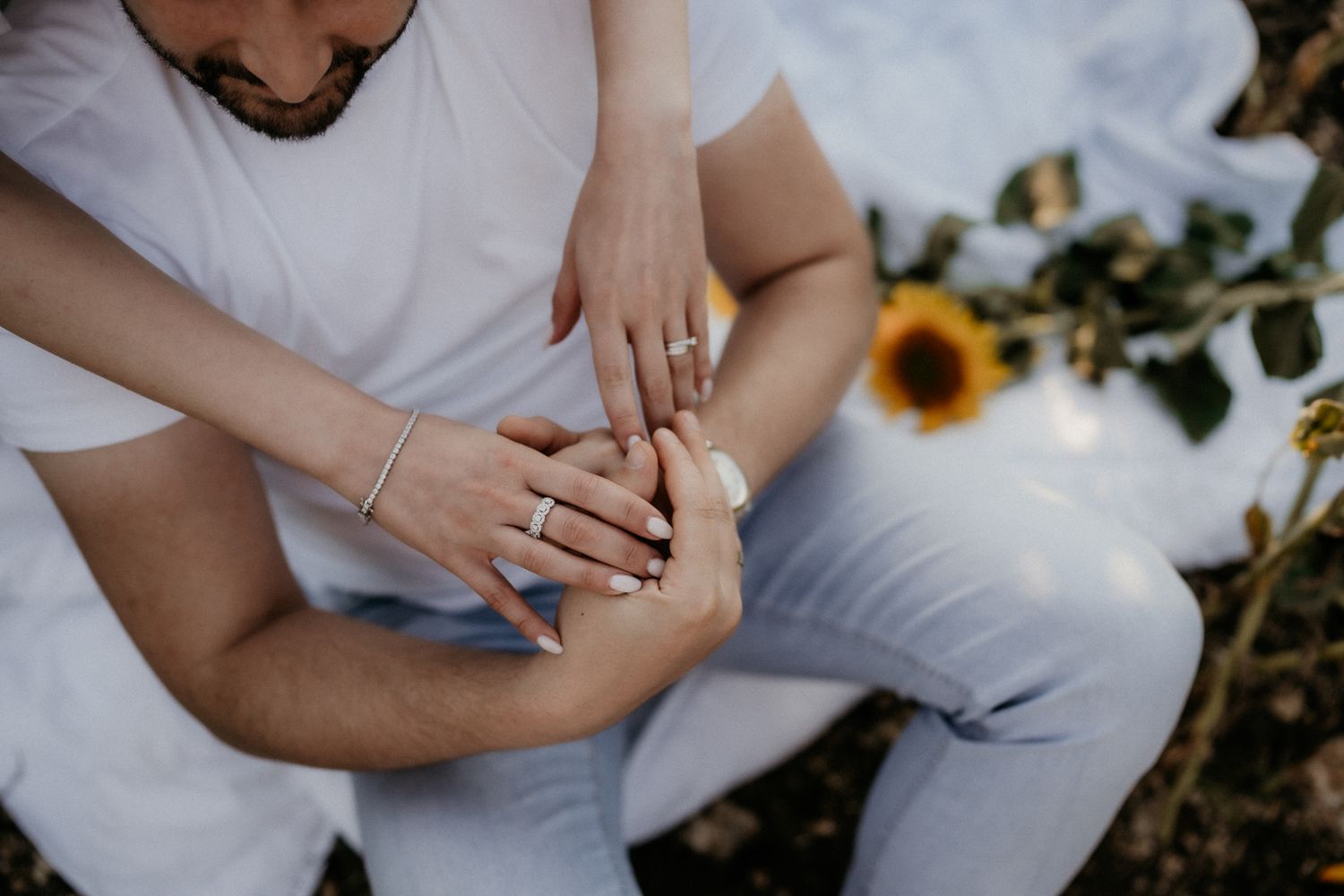Two people dressed in white embrace tenderly among blooming sunflowers.