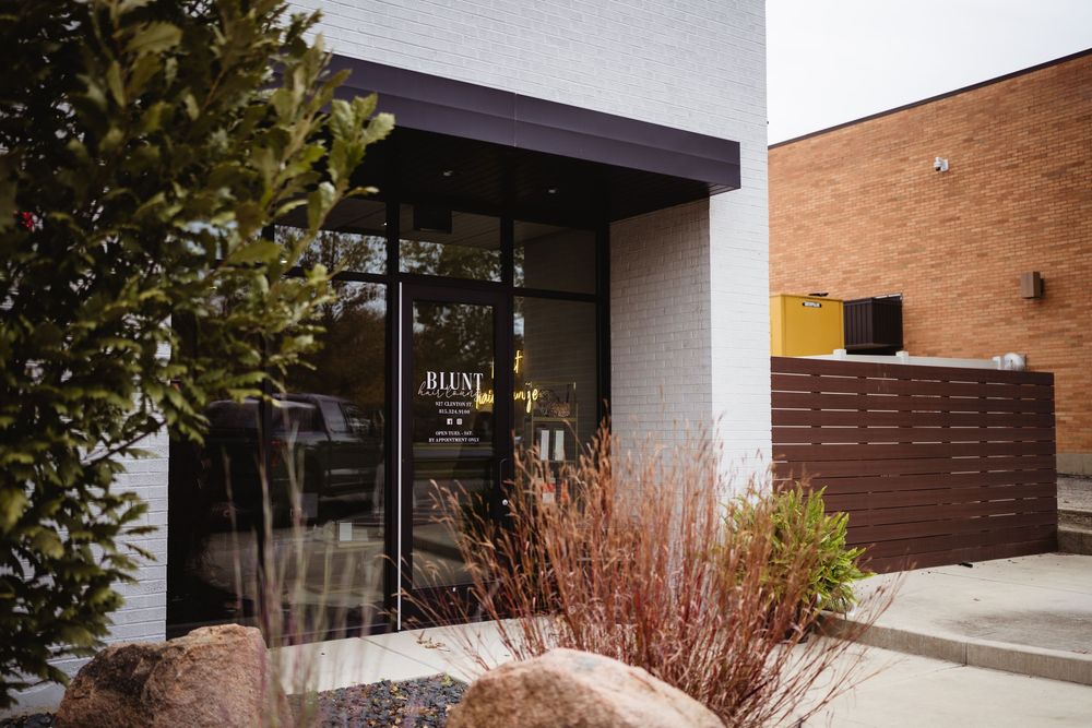 Modern storefront entrance with glass doors, brown wood paneling, and decorative landscaping with bushes and rocks.