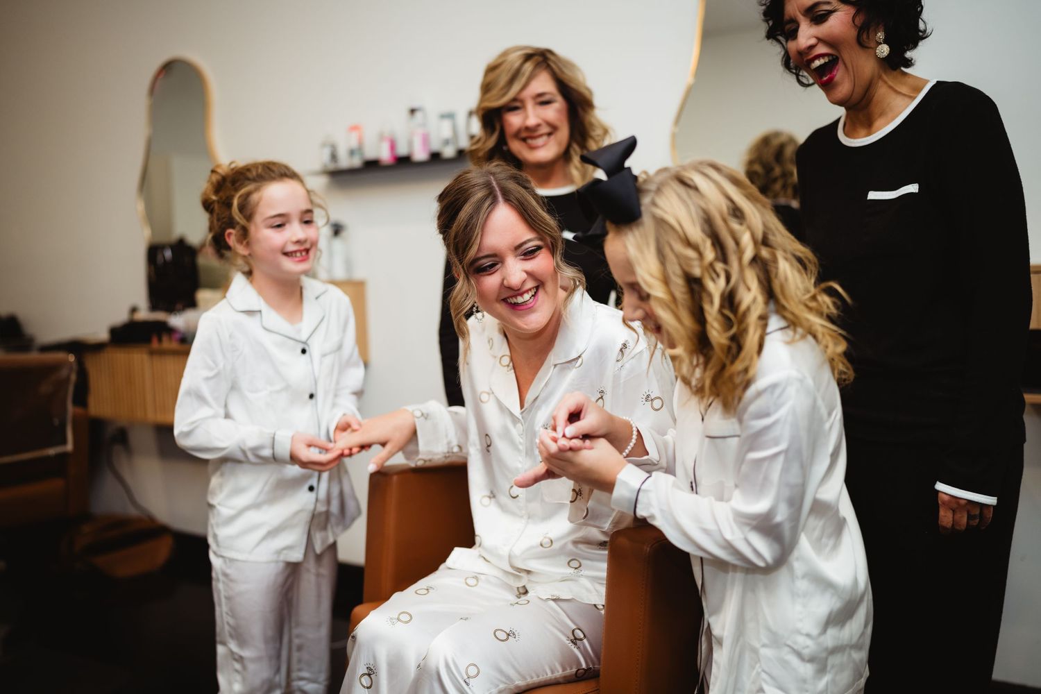 Wedding party members in white robes share laughter and smiles while getting ready.