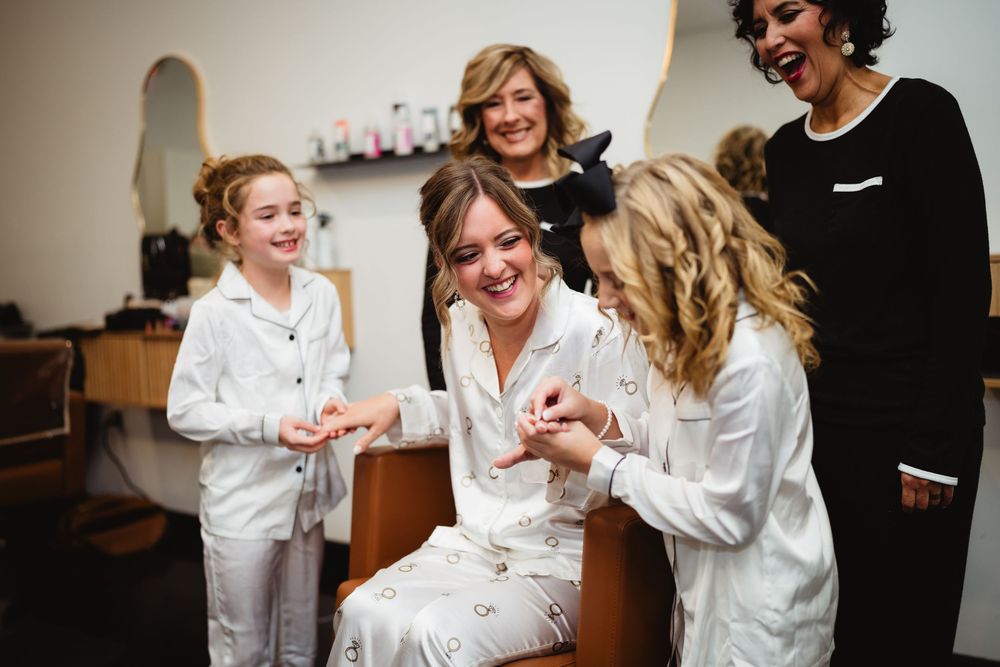 Wedding party members in white robes share laughter and smiles while getting ready.
