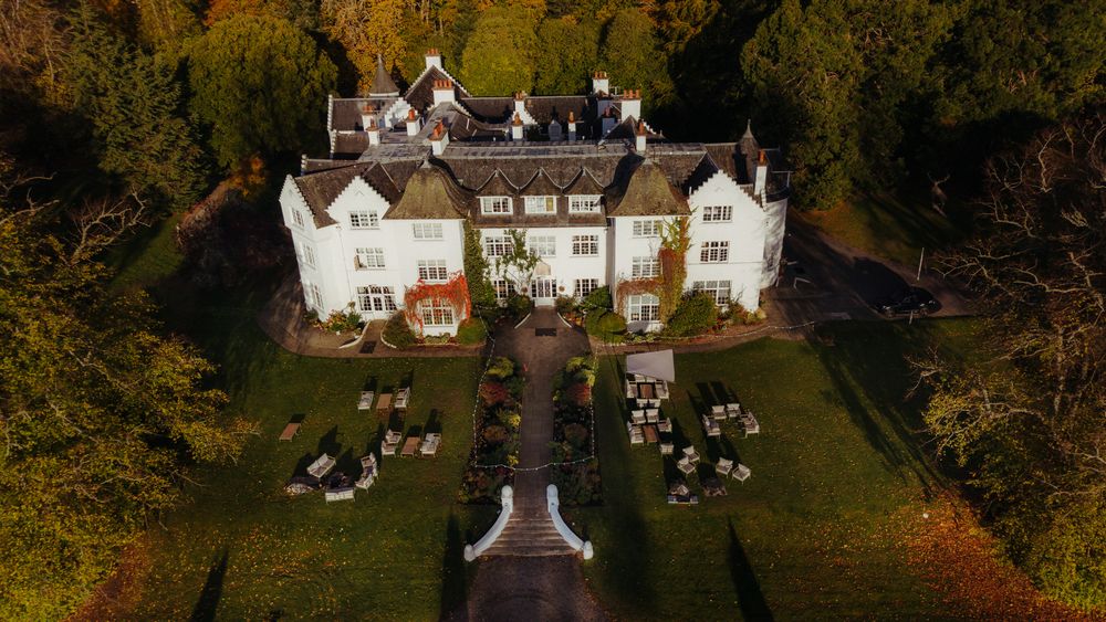Aerial view of a large white mansion estate with landscaped gardens and autumn trees surrounding the property.