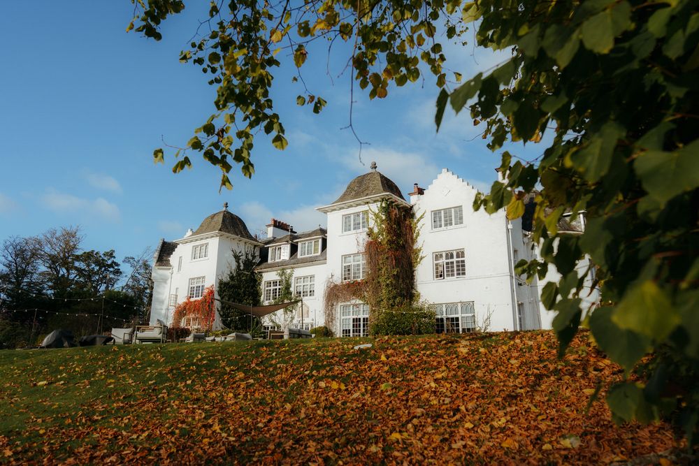White houses with peaked roofs sit atop a hillside covered in vibrant orange autumn foliage.