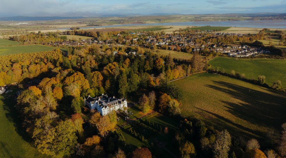 Panoramic aerial view of rolling countryside with autumn trees and scattered buildings in golden afternoon light.