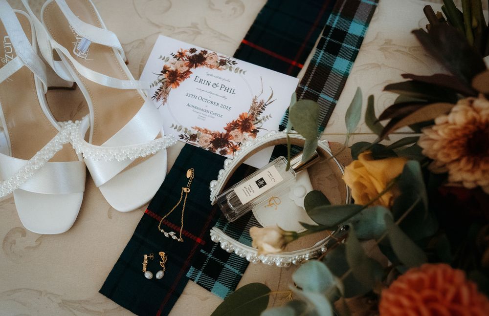 Wedding accessories including white shoes, plaid fabric, and peach-colored flowers arranged on a light beige surface.