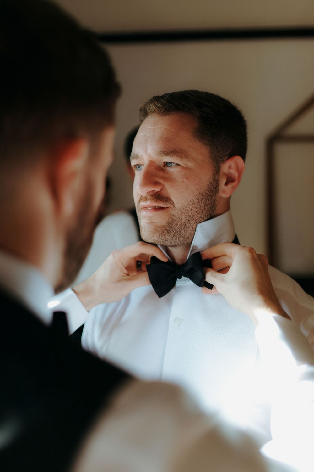 A sequence of close-up shots showing someone adjusting a black bow tie in warm lighting.