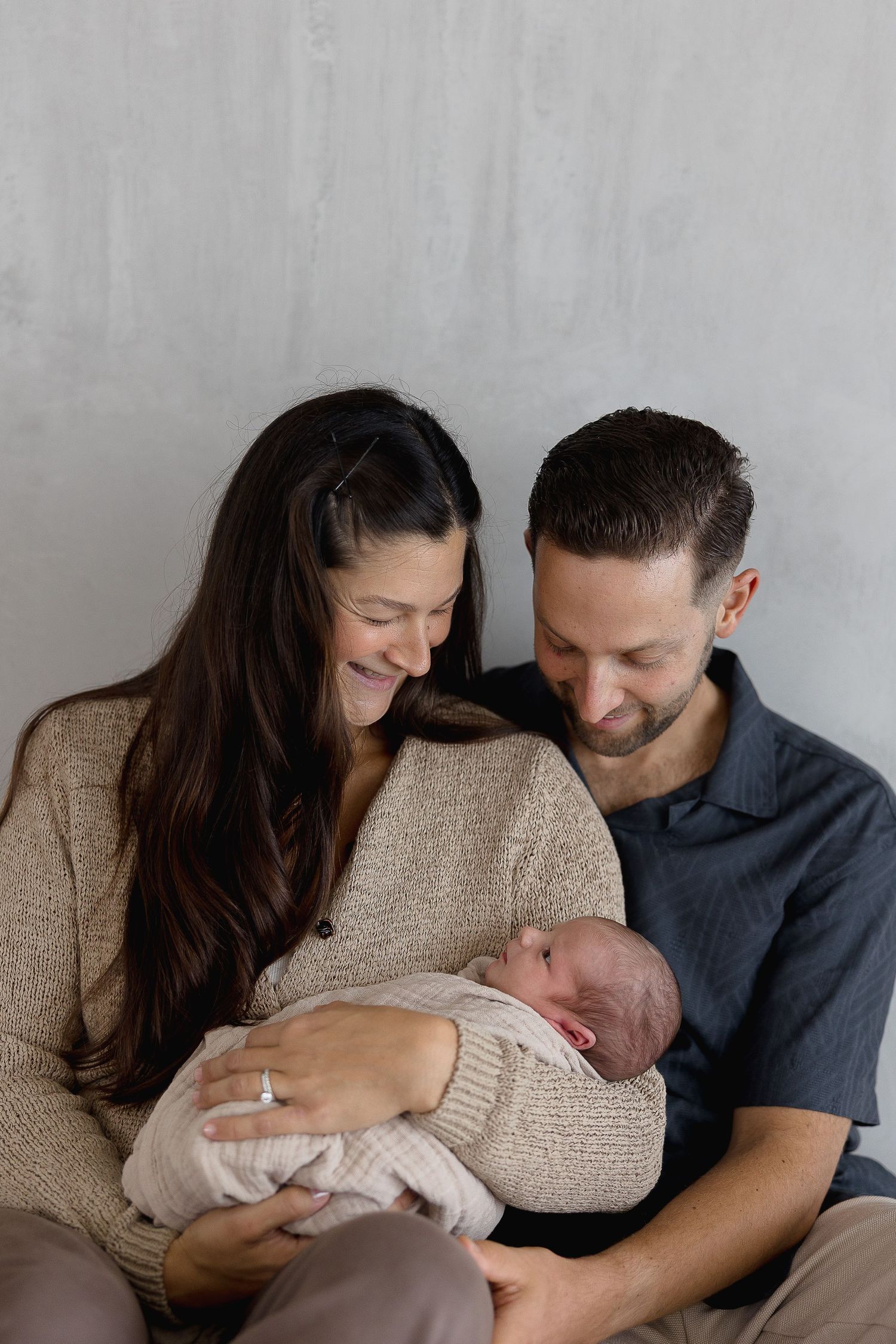 A couple tenderly holds their newborn baby while sitting together on a couch in a series of intimate family photos.