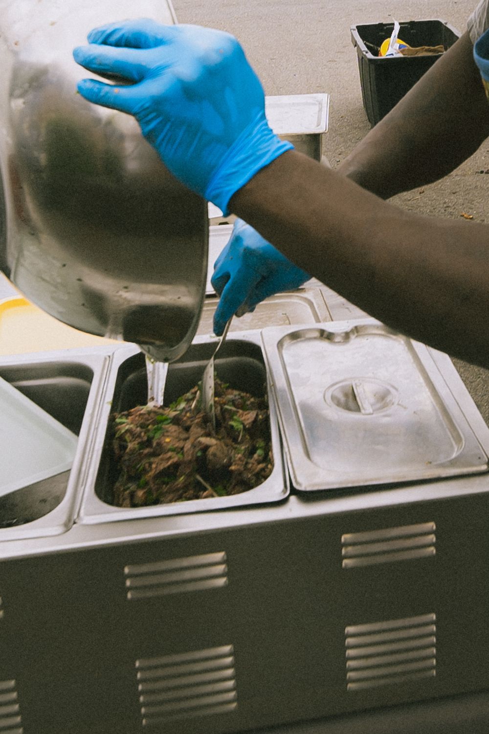 Chef in blue gloves transferring marinated crab into steel food prep containers at outdoor station.