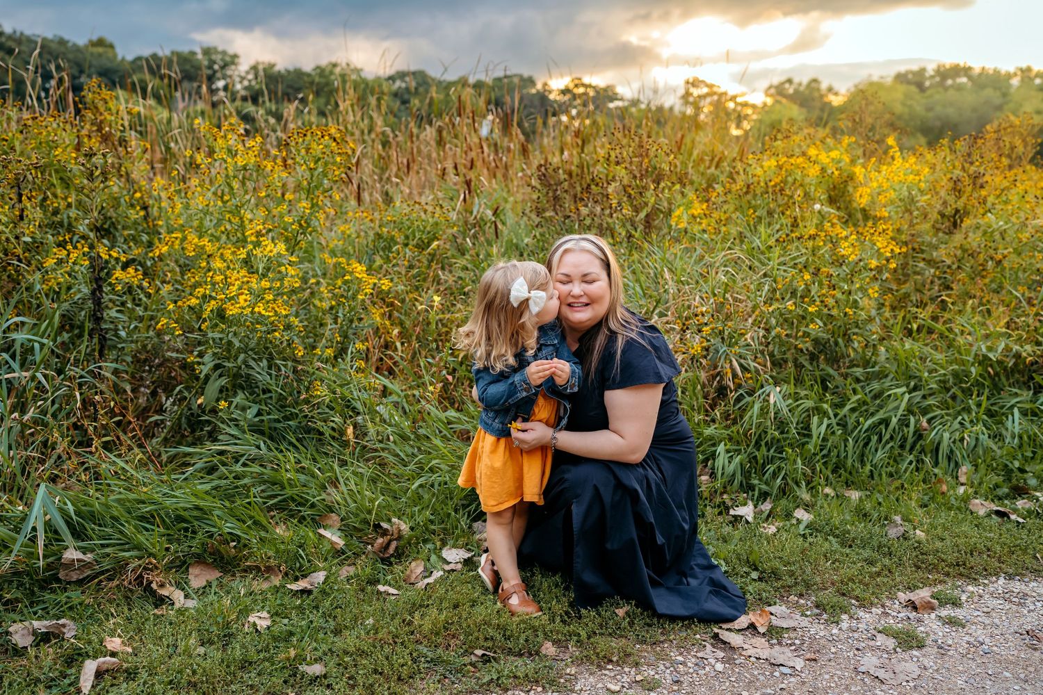 A sunset photoshoot in a field of yellow wildflowers with people sitting along a dirt path.