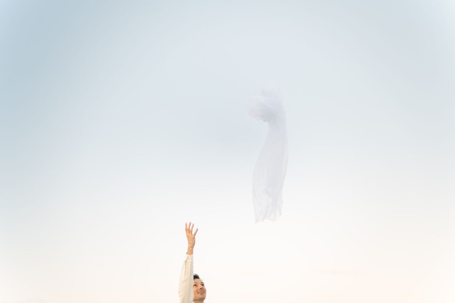 A person stands on a beach with arms raised triumphantly against a bright, misty sky.