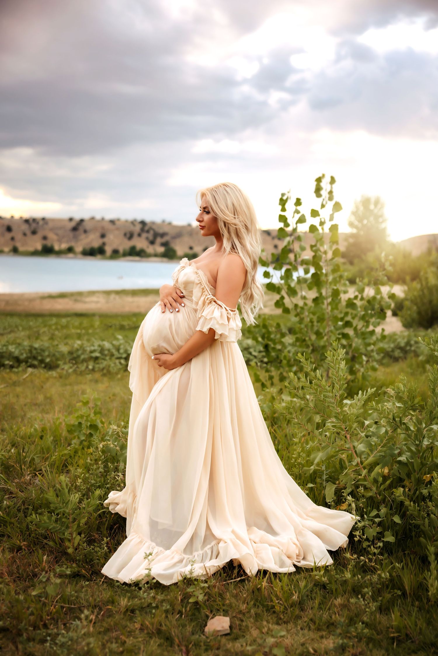 A person in a flowing cream-colored dress poses gracefully in a sunlit meadow at golden hour.