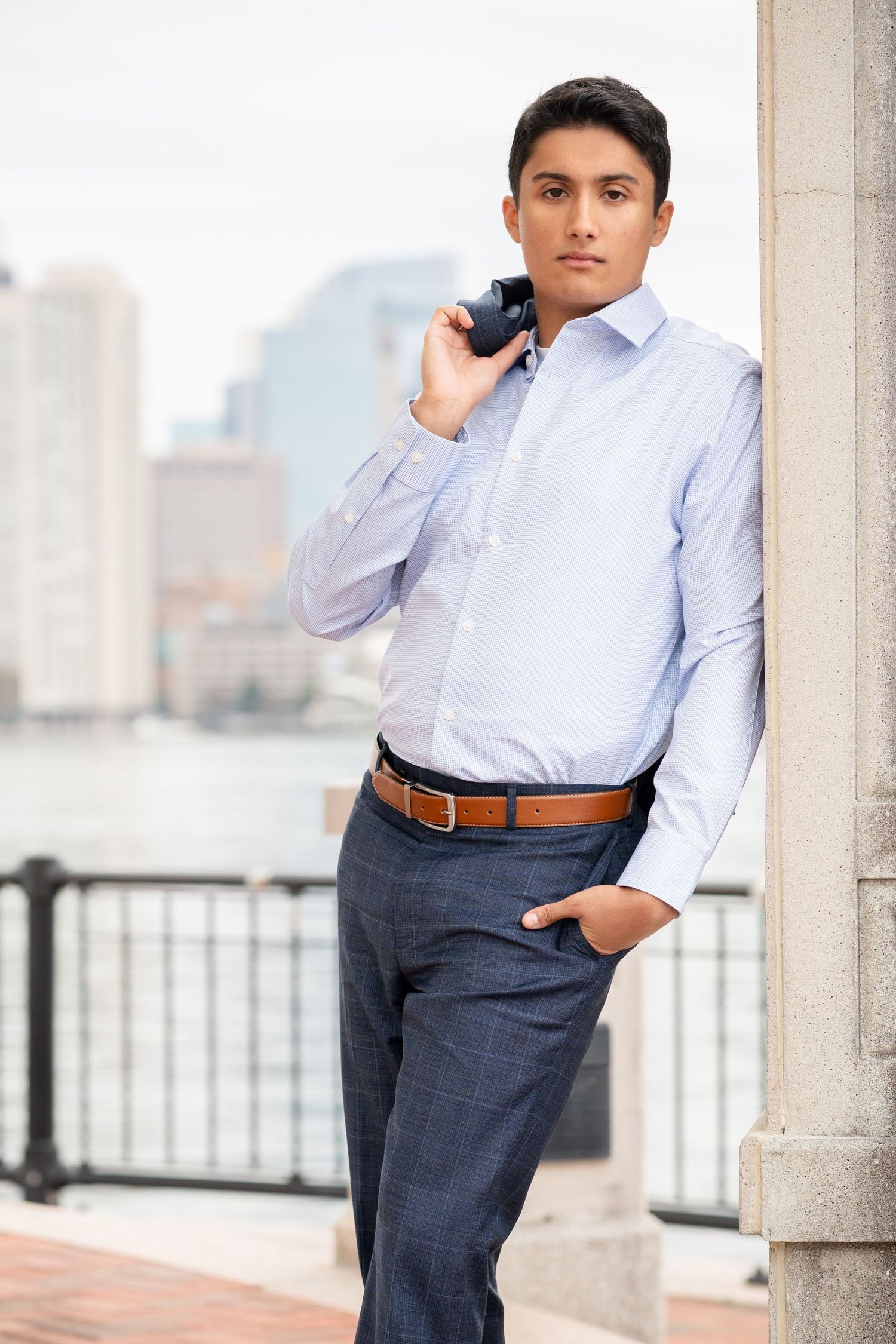 Professional portrait of person in light blue dress shirt and navy slacks posing against urban backdrop with columns.