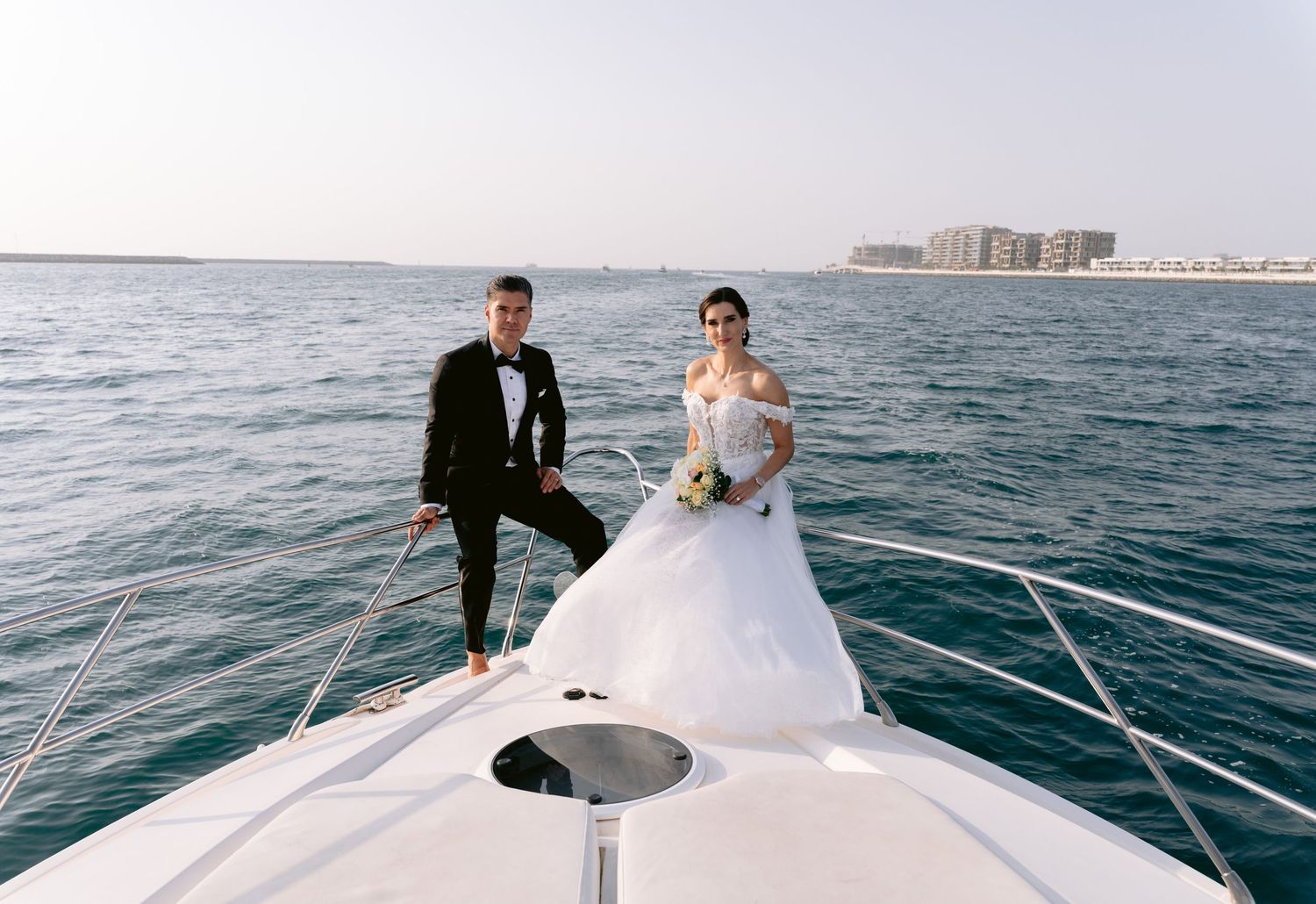Wedding party celebrates on a luxury yacht sailing across blue ocean waters with Dubai skyline in background.