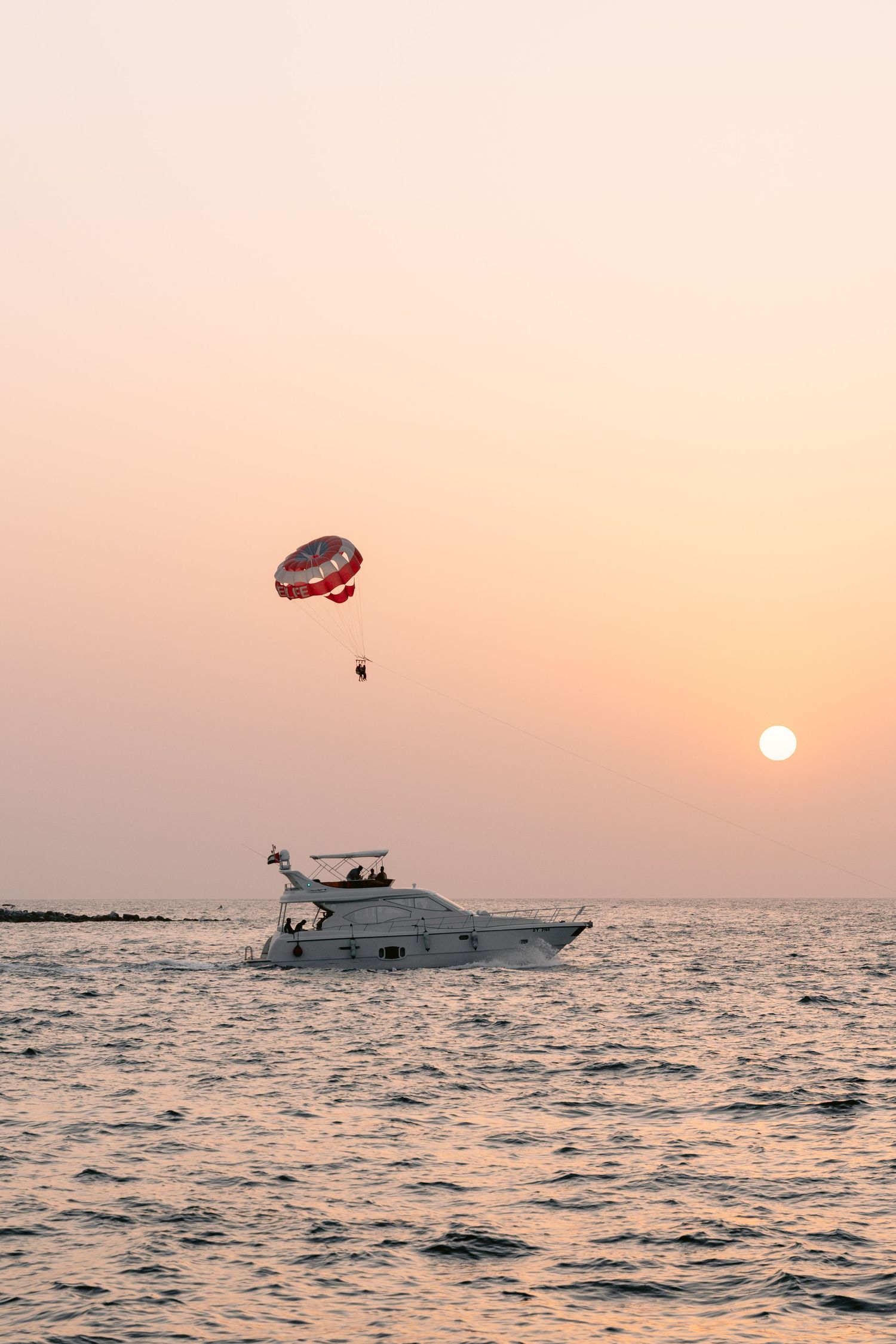 A parasailing boat cruises along the ocean horizon during a vibrant sunset with orange sky over calm waters.